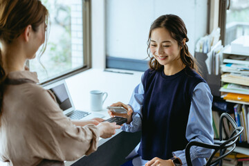 Obraz premium カフェ（コワーキングスペース）でスマホ決済をする女性