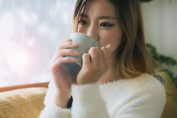 ソファでコーヒーを飲みながらリラックスする女性