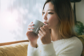 ソファでコーヒーを飲みながらリラックスする女性