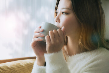 ソファでコーヒーを飲みながらリラックスする女性