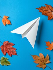 A paper airplane rests on a vibrant blue surface, surrounded by colorful autumn leaves, creating a whimsical and playful scene.