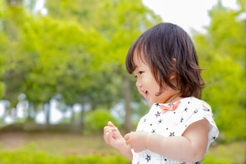 新緑の樹木を背景に笑顔で踊る幼い女の子。育児,教育,躾,愛情,幸せなイメージ
