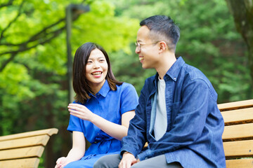 公園のベンチで談笑する若いカップル 