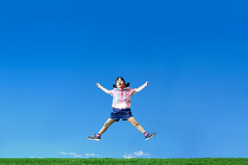 Obraz premium 青空を背景に手足を広げジャンプをする幼い女の子1人