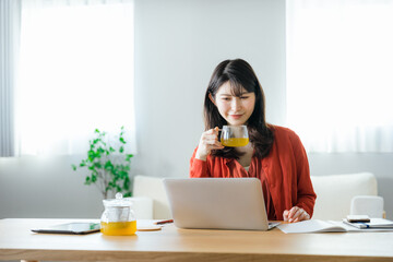 自宅のノートパソコンを見ながらリラックスした表情で紅茶を飲む20代から30代の日本人の女性