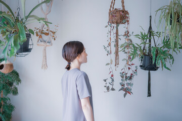 明るい植物のある室内でどこかを見つめるワンピース姿の日本人女性