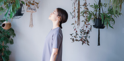 明るい植物のある室内で目を瞑るワンピース姿の日本人女性