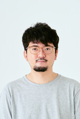 Obraz premium 白背景で眼鏡をかけた髭を生やしたカメラ目線の30代の1人の日本人男性の人物の上半身の正面