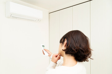 エアコンのリモコン操作をする女性
