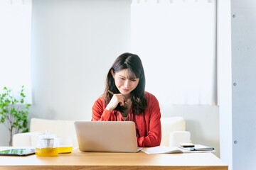 自宅のソファー前のローテーブルのノートパソコンで休日にオンライン講座を受講する30代の1人の女性