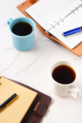 淹れたてのコーヒーが入ったふたつのマグカップとふたつのシステム手帳で、ふたりがコーヒーを飲みながら仕事の打ち合わせをしているイメージ
