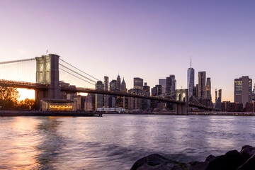 A panoramic sunset view of the Brooklyn Bridge stretching towards Manhattan