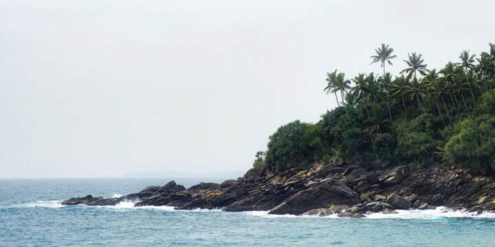 A scenic view of the rocky coastline and lush palm trees in Hiriketiya, Sri Lanka. Perfect for themes of nature, travel, and tropical landscapes. High-quality image ideal for promotional and editorial