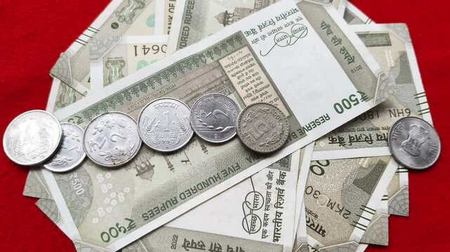 Coins fall on top of indian five hundred rupees (INR) currency notes or banknotes isolated on table background. India tax, bank deposit, loan and inflation concept. Closeup top view.