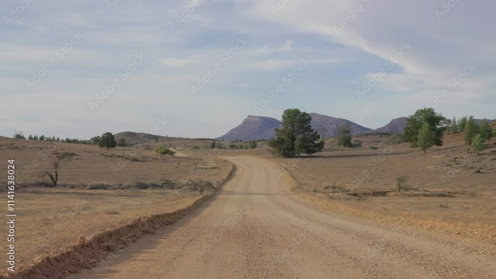 Poster a dirt path cuts through the australian outback, leading the eye towards a distant mountain range in