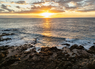 Golden sunset in south of Tenerife, Atlantic ocean waves crash on the rocky beach, horizon over water