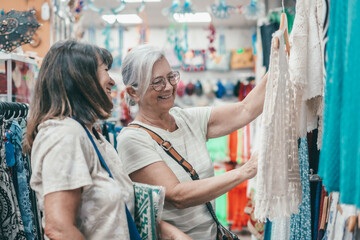 Two smiling senior women looking at clothes while shopping in a store. Consumerism concept