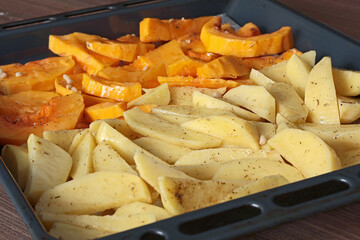 Sliced potatoes and pumpkin with pine nuts and spices on baking tray. Raw vegetables for baking. Healthy food in kitchen at home. Natural farm local products. 