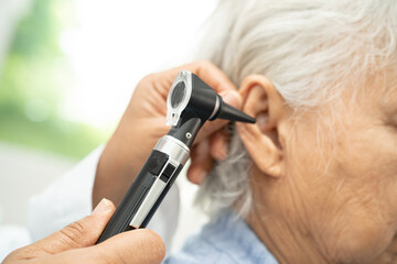 Audiologist or ENT doctor use otoscope checking ear of asian senior woman patient treating hearing...