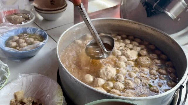 Pouring hot meatballs into a bowl with a plastic wrap base using a round spoon from a hot pot at a meatball vendor's cart. Meatballs are a popular food in Indonesia