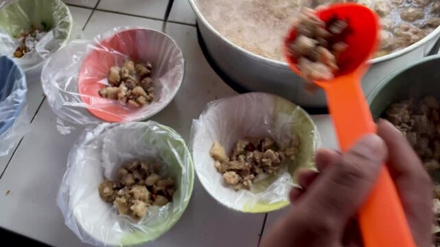 Pouring hot meatballs into a bowl with a plastic wrap base using a round spoon from a hot pot at a meatball vendor's cart. Meatballs are a popular food in Indonesia
