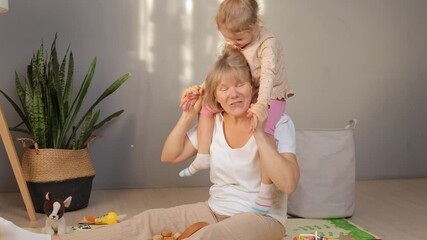 A grandmother enjoys playful moments with her granddaughter, who is sitting on her shoulders. They are surrounded by toys and a warm atmosphere in a simple, inviting room