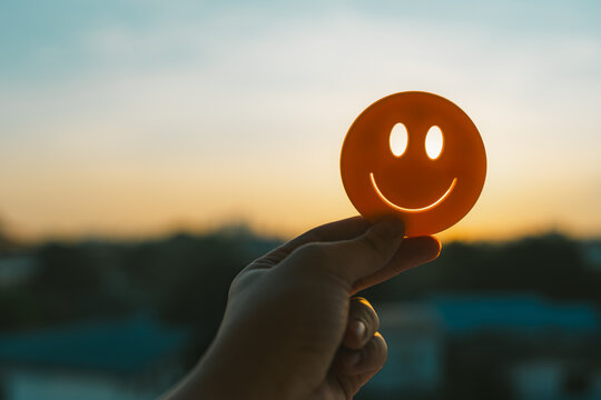 A person holds up a yellow paper with a smiley face towards the morning sun to encourage himself on a bright day. Concept of good mental health, depression treatment and self-empowerment.