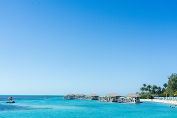 Tropical beach scene with huts and clear blue water.