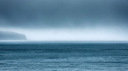 Misty ocean landscape with a distant landmass under a stormy sky.