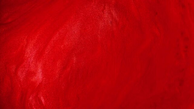 Flowing red abstract glitter background. Liquid paint moves in waves and swirls. Beautiful shiny red texture with sparkles. Metallic paint in motion. Shimmer in slow motion.