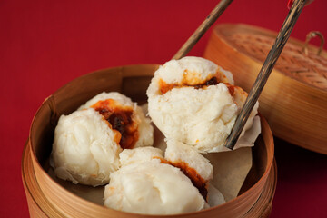 Asian women hand is picking dim sum using wooden chopsticks. Steamed dumplings for Chinese New Year party, isolated on red background.