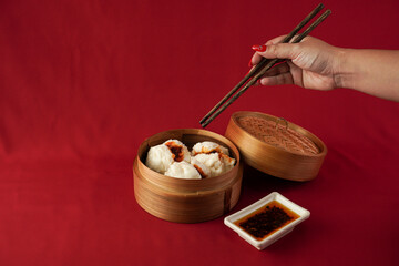 Asian women hand is picking dim sum using wooden chopsticks. Steamed dumplings for Chinese New Year party, isolated on red background.