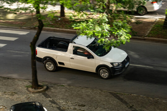 White Volkswagen Saveiro compact pickup truck panning shot, Modern utility vehicle in motion on a city street

