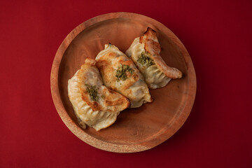 Fried kuotie dim sum on wooden plate isolated on red background. Steamed dumplings for Chinese New...