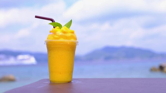 Smoothie made from fresh mango fruits against the backdrop of a seascape. Fruit and yoghurt ice cream decorated with leaves. Glass of tropical dessert close-up.