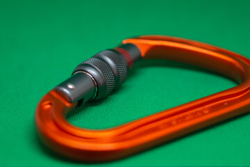 Climbing orange carabiner on a green background close-up, selective focus