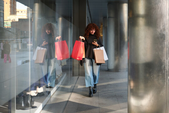 Young woman walking and using phone after shopping spree