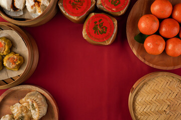 A flat lay photo of a red-clothed table featuring various traditional Chinese New Year dishes such as dim sum, oranges, sticky rice cakes, and red envelopes. (Chinese character 