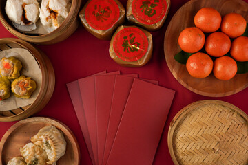A flat lay photo of a red-clothed table featuring various traditional Chinese New Year dishes such as dim sum, oranges, sticky rice cakes, and red envelopes. (Chinese character "fu" means fortune)