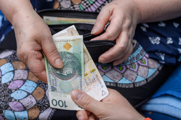 Emerytka seniorka wyjmuje pieniądze z portfela i daje komuś got&oacute;wkę 