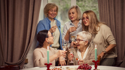 Cozy meeting with friends. Elderly women meeting in warmly-lit restaurant or home, drinking wine, talking and discussing news. Concept of elderly lifestyle, positive emotions