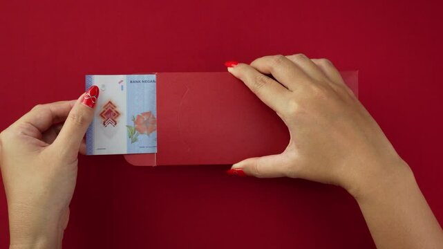 An unlucky Malaysian chinese woman opening a red envelope gift, only to find a very small amount of money inside, one ringgit. Concept for Chinese New Year.