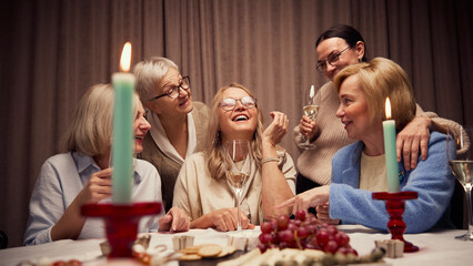 Happy Mothers Day. Elderly women, friends gathering at home, in cozy, warmly-lit living room, laughing, talking and drinking wine. Concept of elderly lifestyle, positive emotions