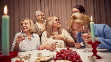 Group of elderly woman, cheerful friends meeting at home, creating cozy moment of friendship and memories, talking and drinking wine. Concept of elderly lifestyle, positive emotions