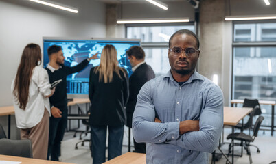 Fototapeta premium African American man is standing against his colleagues. Group of office workers are indoors together
