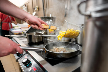 A chef's hand pours pasta into a pan with clams, creating a flavorful dish in a bustling kitchen. Steam rises, highlighting the vibrant cooking environment and culinary action.