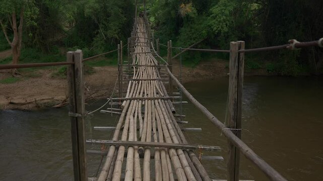 POV shot crossing a rickety bamboo bridge in the jungle across a river.