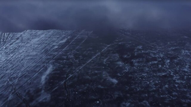 Aerial view of a thin ice layer floating on top of a vast lake during a cloudy and misty morning, tilting up revealing the landscape with mountains in the far distance