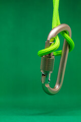Obraz premium Metal climbing carabiner hanging on rope on green background, side view