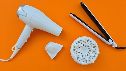 White appliances: hair dryer, nozzles and straightener on an orange background. Devices for...
